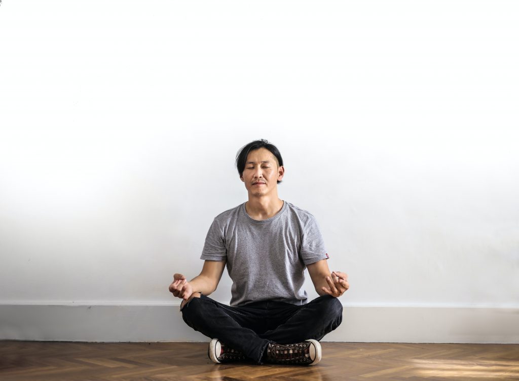 Mindfulness In Sexual Fulfilment: Male Sits Against White Wall Meditating