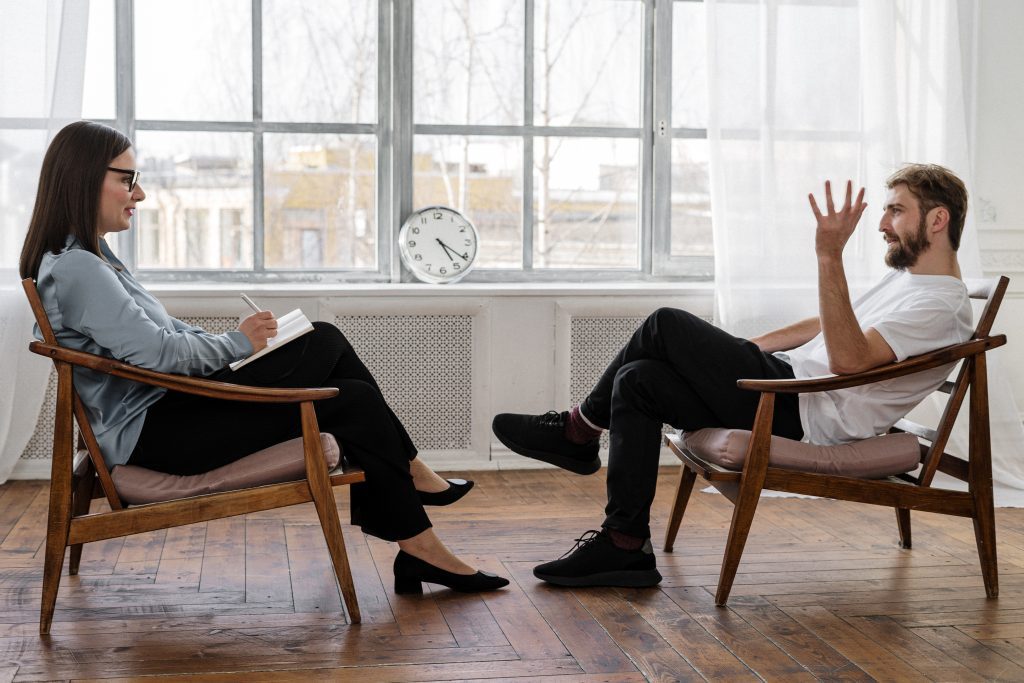 Mindfulness In Sexual Fulfilment: Male Client Sits In Chair Talking To Female Therapist